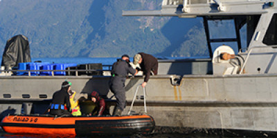 An MPI compliance officer climbs aboard to check the catch records of a commercial cray-fishing vessel while divers in the dinghy prepare to inspect the hull for marine pests.