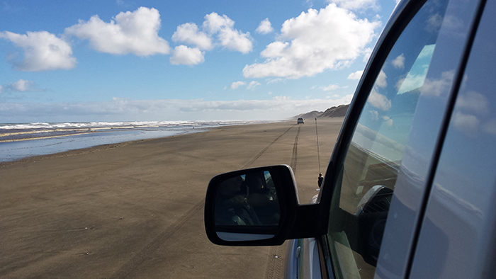 Part of a beach taken from the back window of a car. Part of the car is shown.