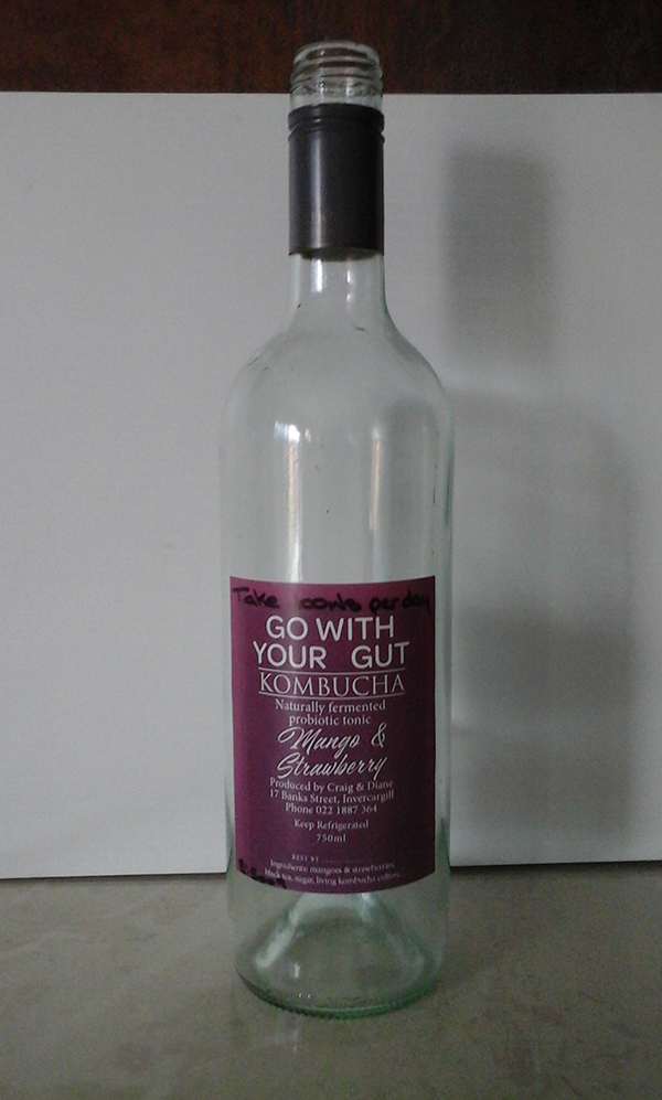 An empty glass bottle of kombucha, mango and strawberry flavour.