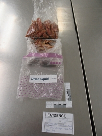 Plastic wrapped bag labelled dried squid next to evidence tag with the description ‘Re-enactment of dried squid package.