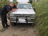 Kyall, in his uniform, bending over the bonnet of a car, writing notes.