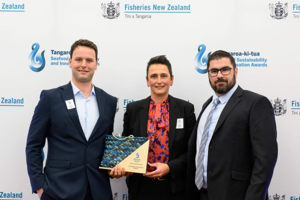 Three people in suits, holding an award.