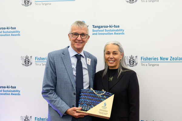 Man and woman holding an award, Fisheries New Zealand branded background.