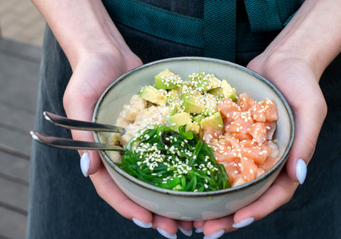 Hands holding poke bowl with raw fish.