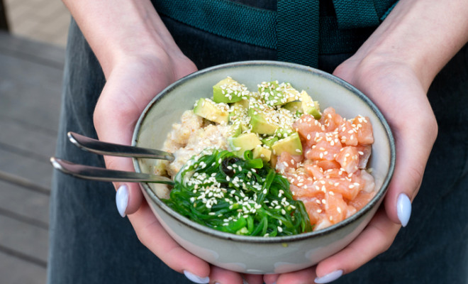 A woman holds a traditional Hawaiian poke bowl with fish in her hands. Hawaiian and Japanese cuisine