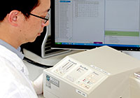 Scientist analysing real-time PCR data on a monitor next to PCR machine