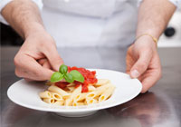 chef adding basil leaf to tomatoes on plate of pasta