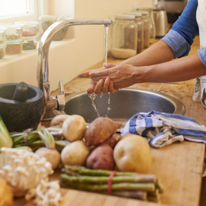 a person washes their hands in a kitchen sink, vegetables are on the bench top