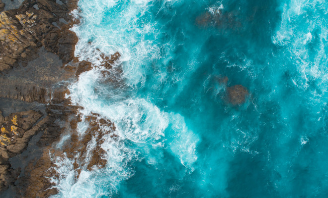 Bird's view of rugged rocky coast battered by bright blue sea.