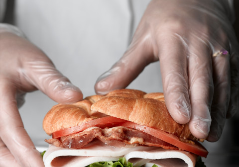 Gloved hands preparing sandwich.